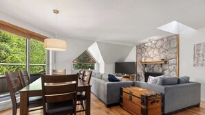 A modern living room with a dining table, sofa, and a stone fireplace.
