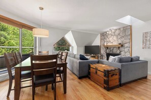 A modern living room with a dining table, sofa, and a stone fireplace.