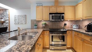A kitchen with granite countertops, stainless steel appliances, wooden cabinets, and a stone accent wall.