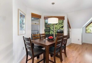 Ein Essbereich mit Holztisch, Stühlen, einer Hängeleuchte und Blick auf Grünflächen.