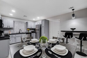 Una cucina moderna con mobili bianchi, elettrodomestici in acciaio inossidabile e un'area pranzo con tavolo apparecchiato per quattro persone.