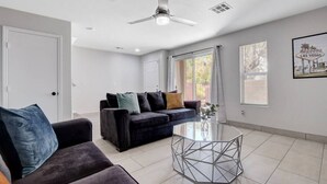 Ein modernes Wohnzimmer mit einem dunkelgrauen Sofa, einem Glastisch und einem Deckenventilator.
