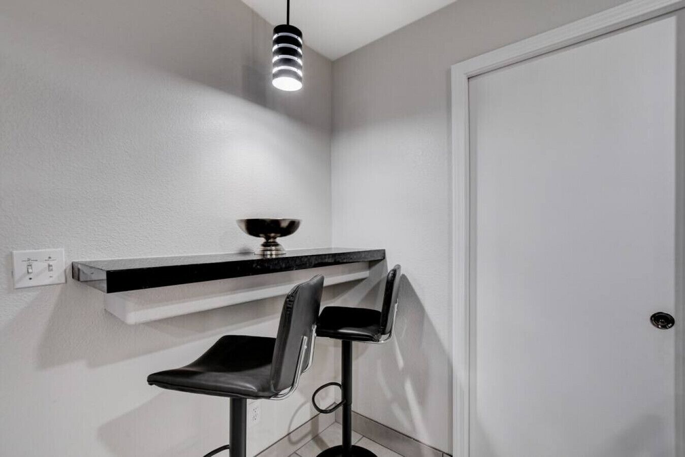 A modern bathroom with a white wall, a black countertop, a mirror, and two black bar stools.