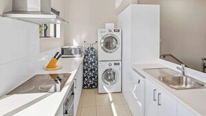 Una cucina compatta con forno a microonde integrato, lavatrice a doppia apertura, lavello in acciaio inossidabile e piano cottura moderno.