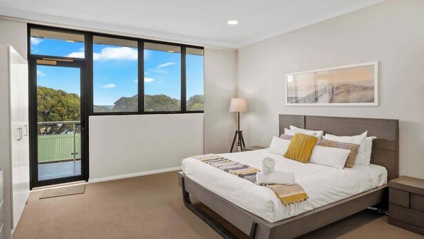 Una camera d'hotel con un letto grande, una lampada da terra, un quadro incorniciato appeso al muro e un balcone con vista sul verde.