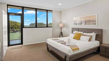 A hotel room with a large bed, a standing lamp, a framed picture on the wall, and a balcony with a view of greenery.