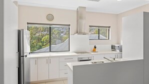 Una cucina moderna con mobili bianchi, un frigorifero in acciaio inossidabile, un forno a microonde e un'ampia finestra con vista sulla città.