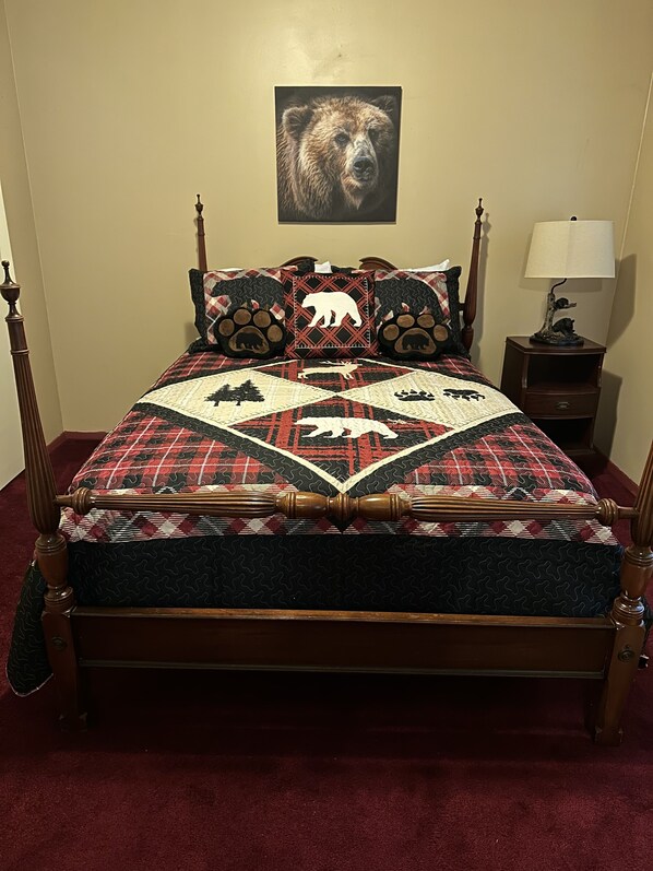 A bed with a quilt featuring animal patterns, a wooden headboard, a bedside table with a lamp, and a bear-themed pillow.
