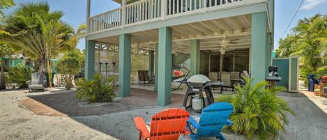A covered outdoor area with two Adirondack chairs, a barbecue grill, and a patio with tables and chairs.