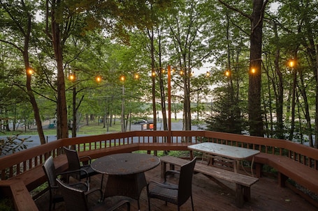 An outdoor deck with a round table and chairs, surrounded by trees and string lights.