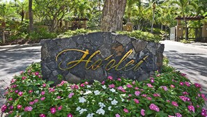 Ein Steinschild mit der Aufschrift "Hotel", umgeben von einem Blumenbeet mit rosa und weißen Blumen.