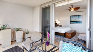 Ein Hotelzimmer mit einem Bett, einer Sitzecke mit Stuhl und Tisch, einem kleinen Sofa, einer Holzbank und einem Balkon mit Topfpflanzen.