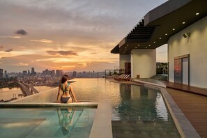 A woman sitting by an infinity pool with a city skyline in the background.