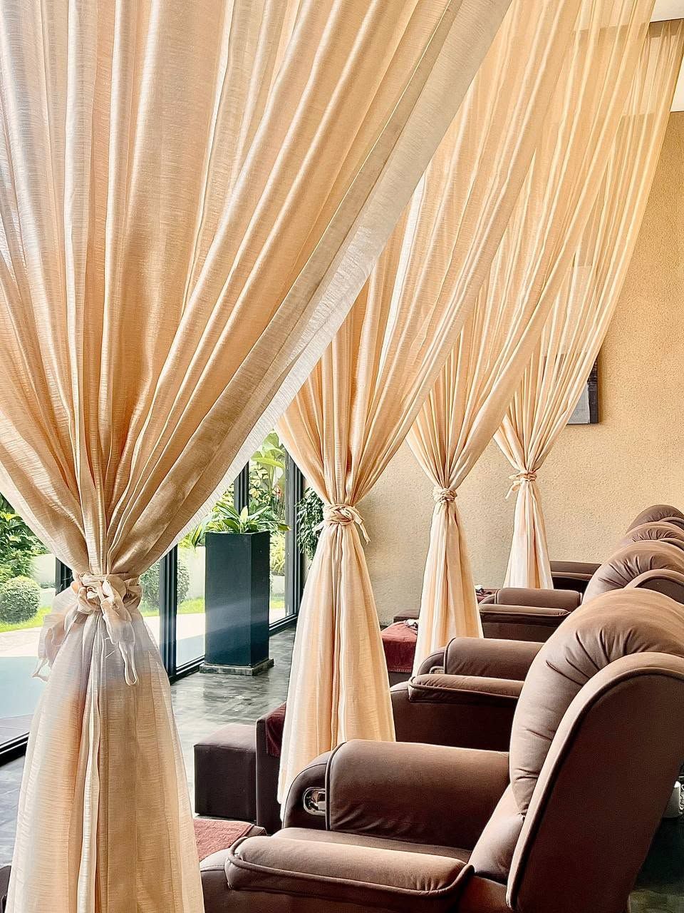 A room with three reclining chairs and beige curtains tied at the top.