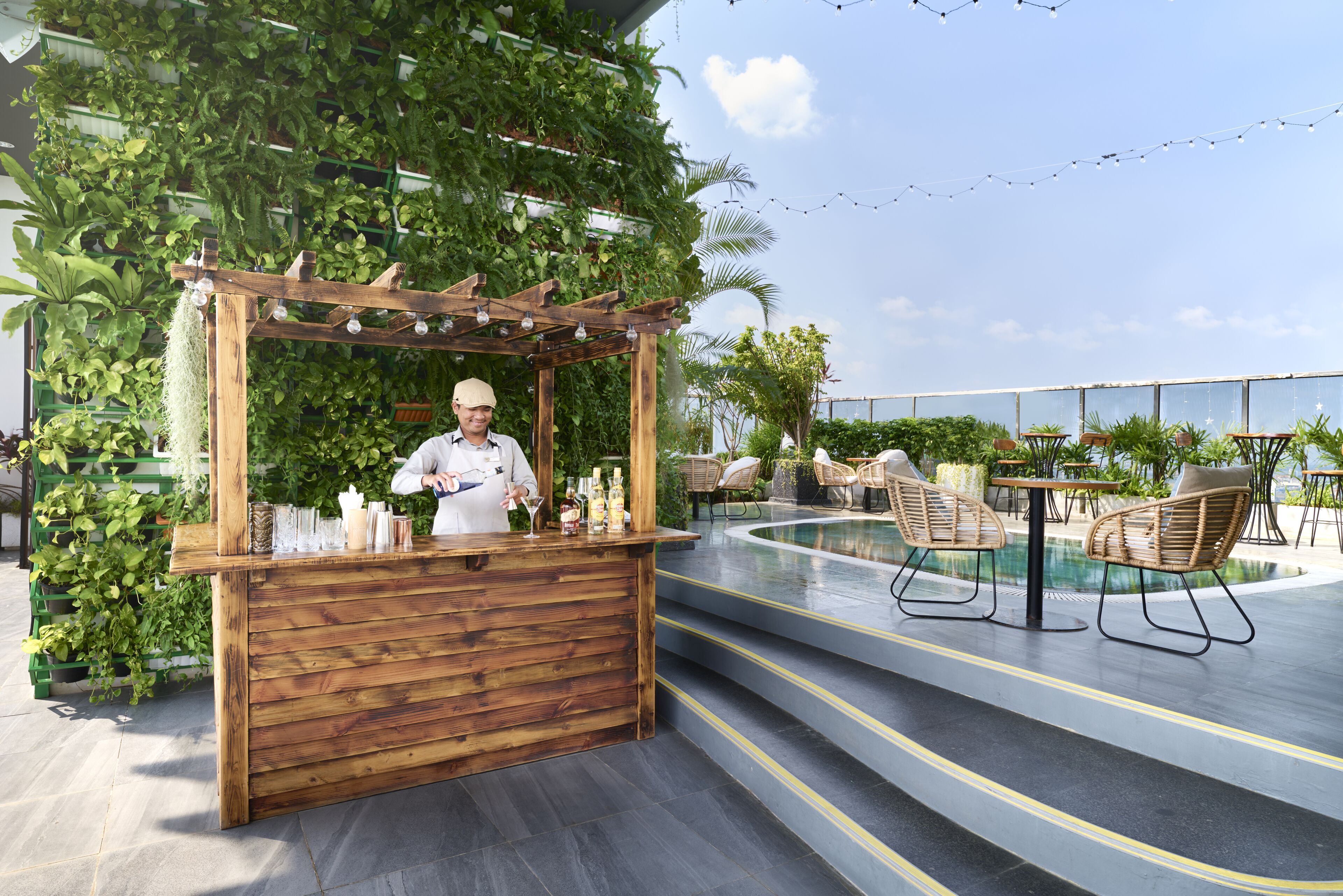 A bar area with a wooden counter, surrounded by lush greenery and outdoor seating.
