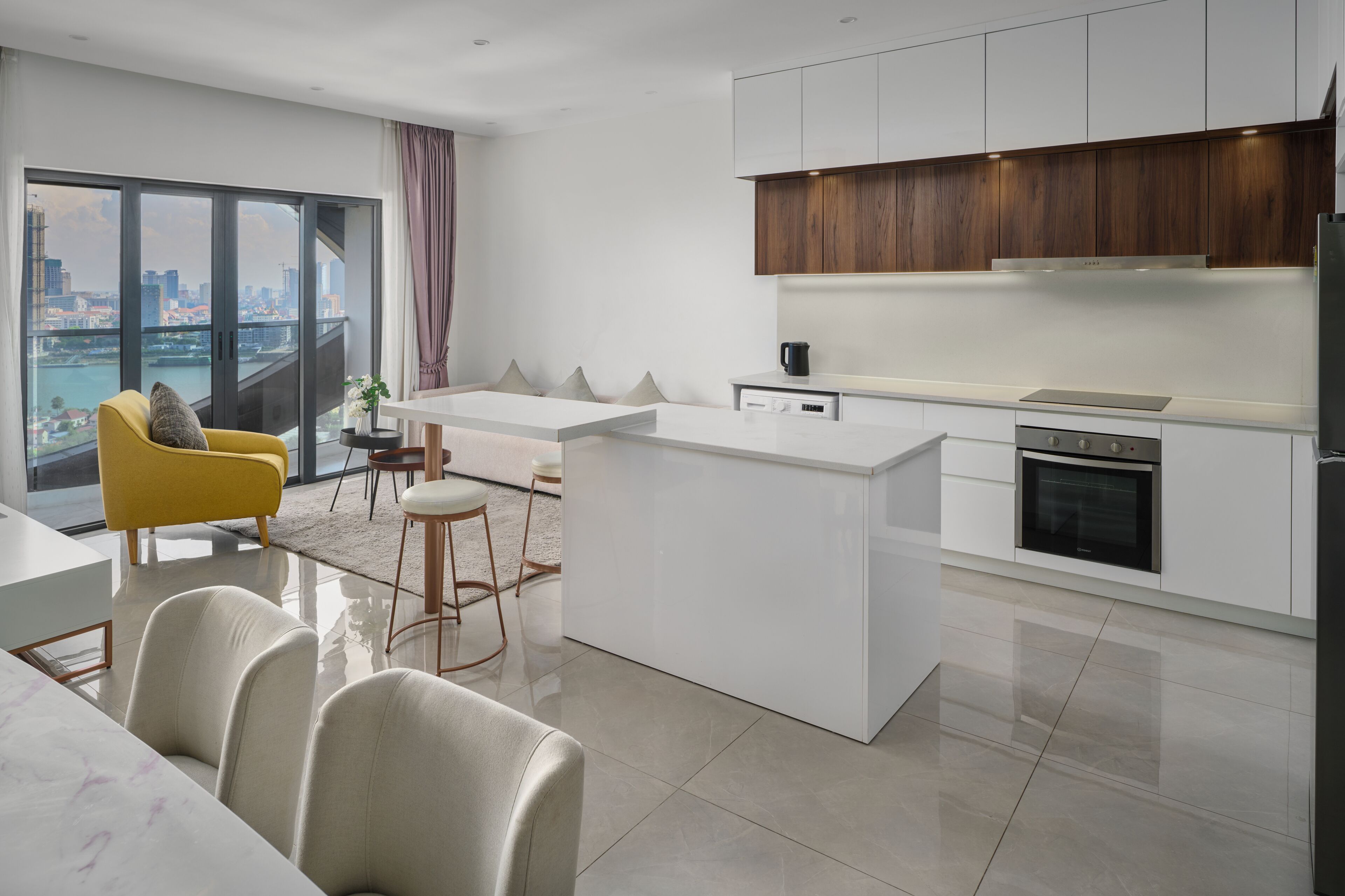 A modern kitchen with a central island, white cabinetry, and a view of the city through large windows.
