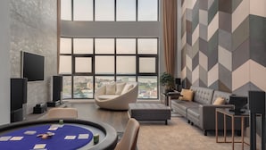 A modern living room with a pool table, comfortable seating, and large windows offering a city view. - THE PENINSULA PHNOM PENH (Phnom Penh)
