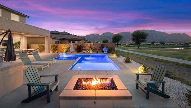 A modern outdoor pool area with two pools, lounge chairs, and a fire pit.