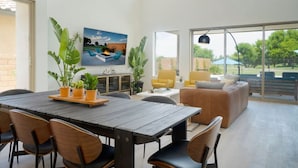 A spacious living area with a large dining table, comfortable seating, and a view of the outdoors.