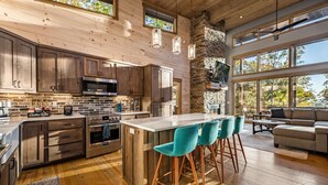 A modern kitchen with wooden cabinets, a large island with bar stools, and a stone fireplace.