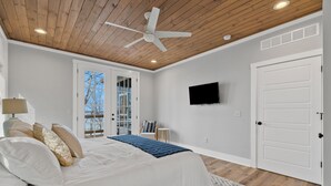 Un dormitorio con cama, ventilador de techo, televisor y puerta.