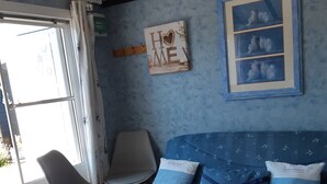 A room with a blue bed, two chairs, a window with curtains, and a wall with a framed picture and a sign that says "HOME". - 5 minutes from the beach, campsite, very quiet (Le Coq)
