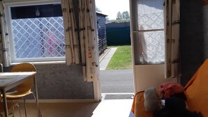 A room with a bed, a table, and a chair. There is a window with curtains, a clock on the wall, and a view of the outside. - 5 minutes from the beach, campsite, very quiet (Le Coq)