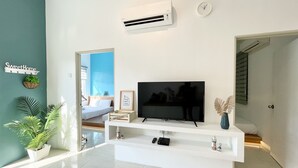 Un salon moderne avec un téléviseur à écran plat posé sur un meuble de télévision blanc, un climatiseur fixé au mur et une horloge murale.