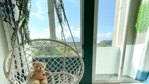 Une pièce avec un fauteuil suspendu en macramé, un tapis moelleux et une vue sur la verdure par la fenêtre.