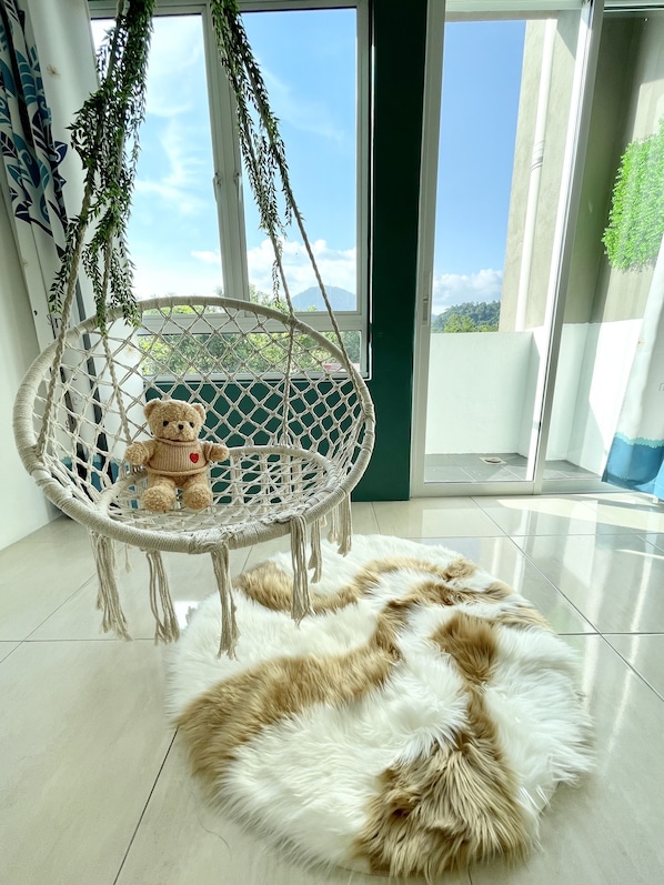 Une pièce avec un fauteuil suspendu en macramé, un tapis moelleux et une vue sur la verdure par la fenêtre.