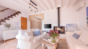 A modern living room with a white sofa, a coffee table with a vase of flowers, a fireplace, and a TV mounted on the wall.