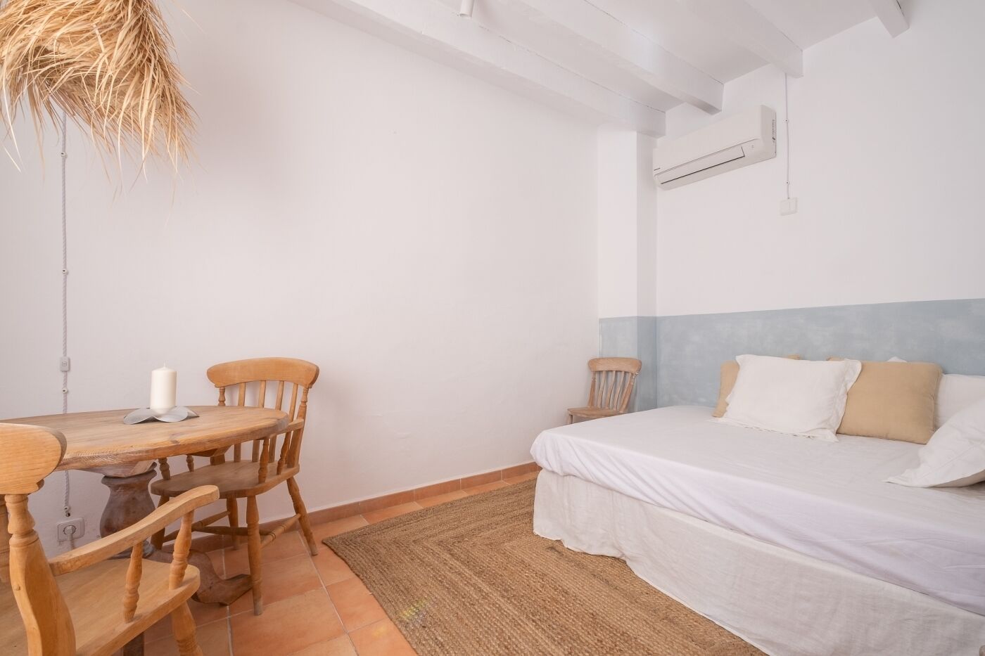 Une chambre à coucher avec un lit, une table en bois avec des chaises et un luminaire suspendu.