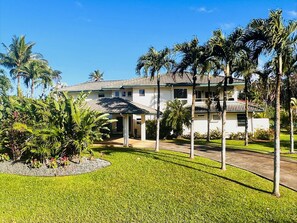 A two-story house with a covered patio, surrounded by palm trees and a well-maintained lawn.