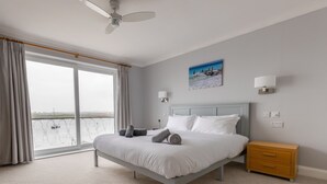 Une chambre à coucher avec un lit, une table de chevet, un ventilateur de plafond, un tableau et une vue sur l’eau.
