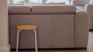 Un salon doté d’une grande fenêtre, d’un canapé, d’un petit tabouret et offrant une vue sur une étendue d’eau où se trouve un bateau.