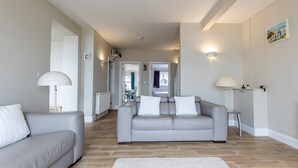 Un salon moderne avec un canapé gris, un fauteuil blanc et un tapis blanc. On y trouve deux lampadaires et un tableau accroché au mur.