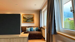 Een knus vertrek met een bed, een bank, een schilderij en een raam met gordijnen.