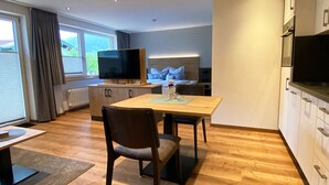 Een moderne woonkamer met een houten eettafel, twee stoelen, een flatscreen-tv en een bank.