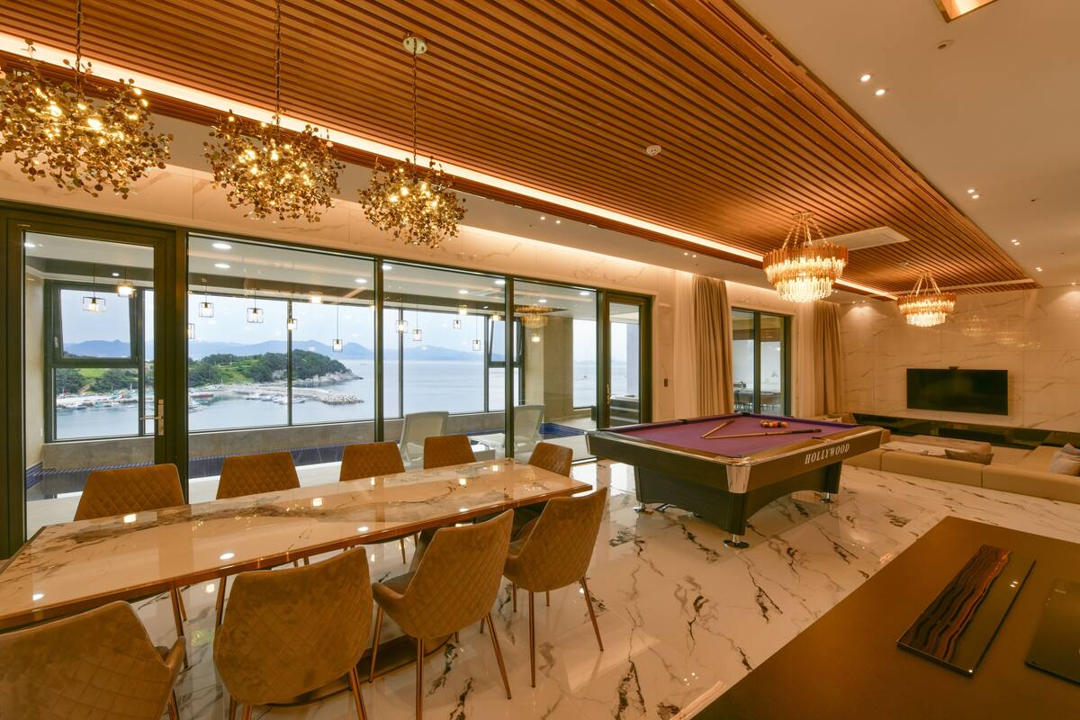 Une pièce moderne équipée d’une table de billard, d’une table à manger avec des chaises, et de grandes fenêtres offrant une vue sur la mer.