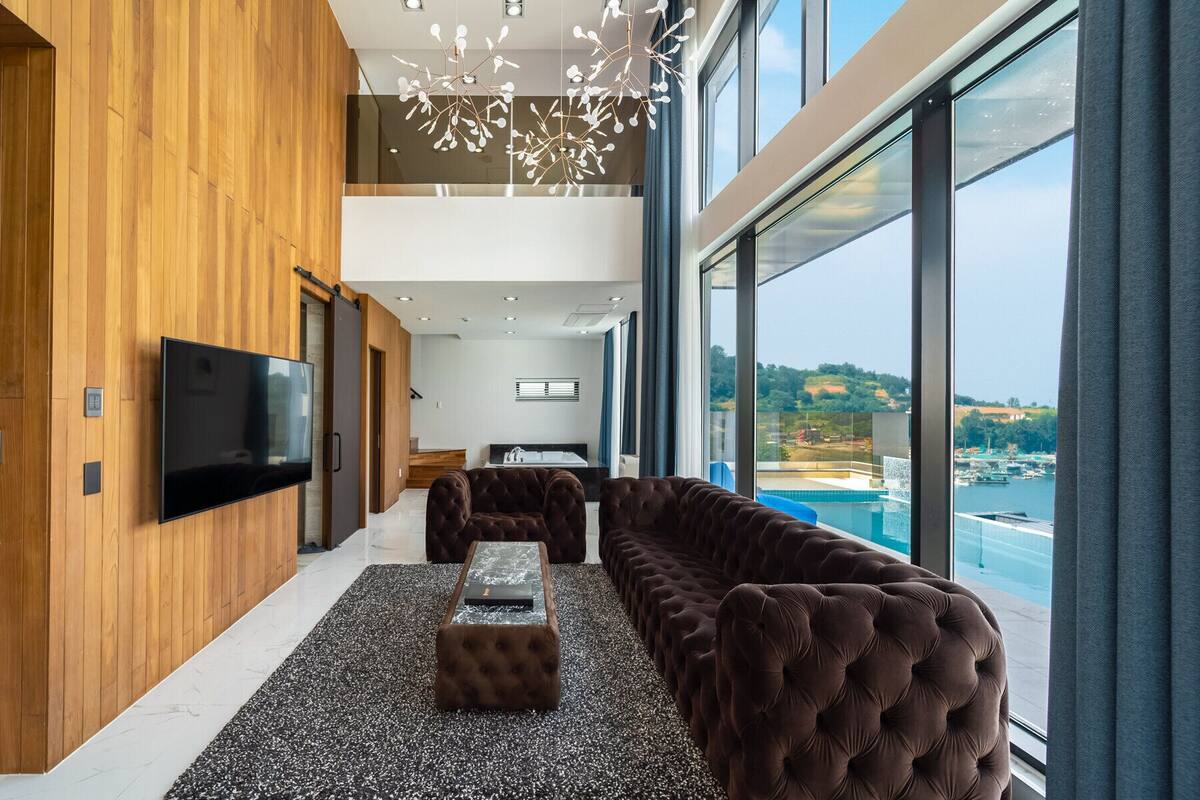 Un intérieur moderne avec un grand téléviseur, des fauteuils confortables, une petite table et une vue sur la mer.
