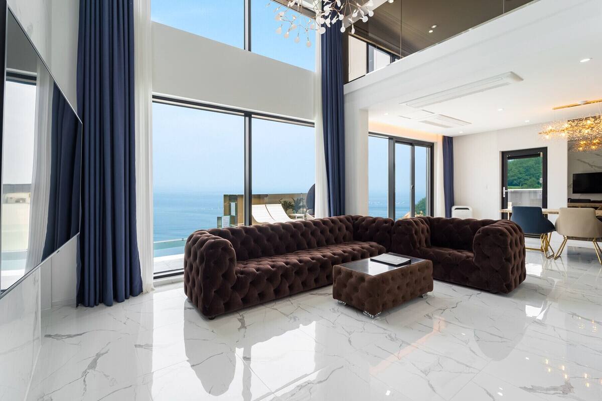 Un salon moderne avec un grand canapé d’angle, une table basse et une vue sur l’océan.