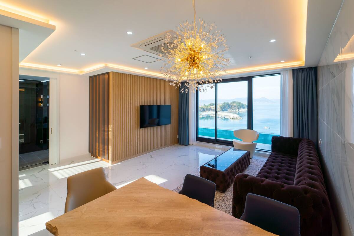 Une chambre d’hôtel moderne dotée d’une grande fenêtre donnant sur la mer, d’un canapé confortable, d’une table à manger et d’un lustre.