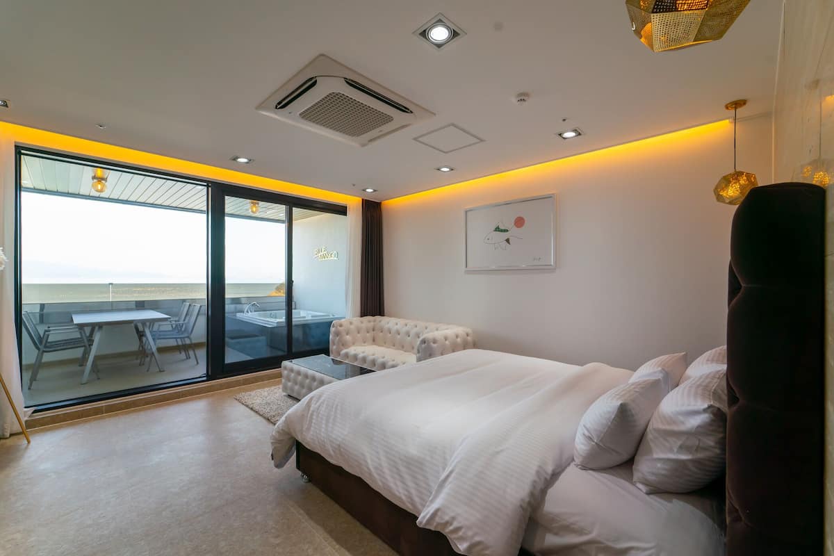 Une chambre moderne dotée d’un grand lit, d’un coin salon avec un fauteuil confortable et d’une vue sur la mer grâce à de grandes portes vitrées.