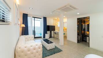 A modern living room with a sofa, a coffee table, and a TV. There is a balcony with a view, a desk, and a chair.