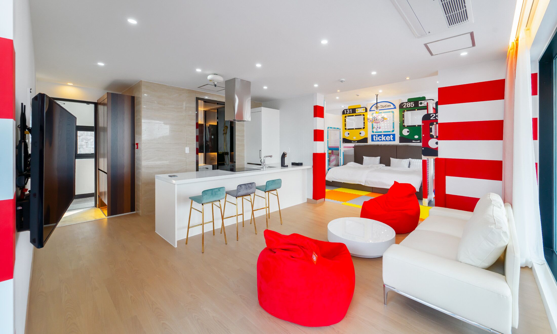A modern living room with a white sofa, red bean bag, and a kitchen area with a central island.