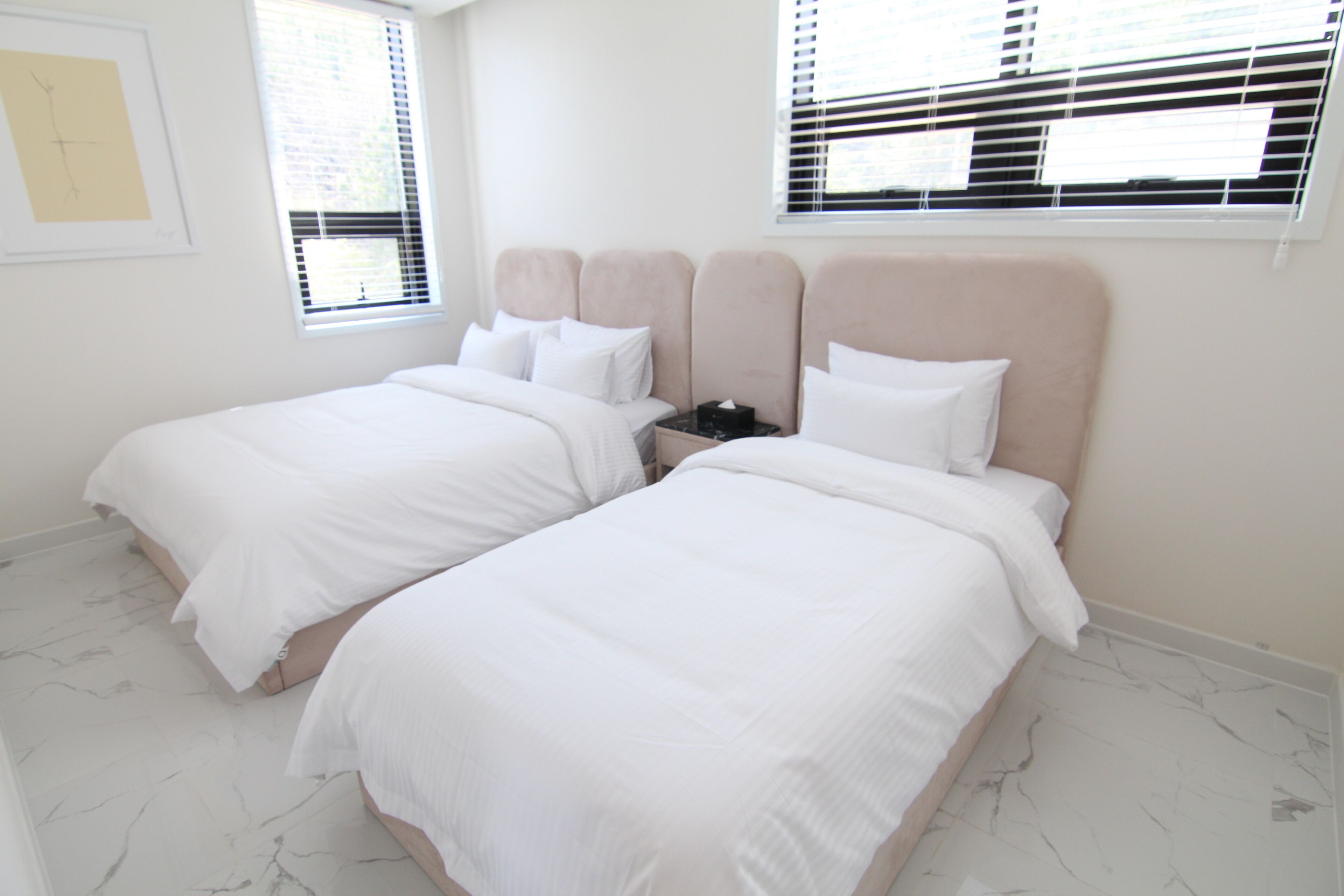 Un dormitorio con dos camas, ropa de cama blanca, suelo de mármol y un cuadro enmarcado en la pared.