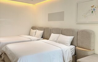 Una habitación de hotel con dos camas, cabeceros, mesitas de noche y una obra de arte enmarcada en la pared.