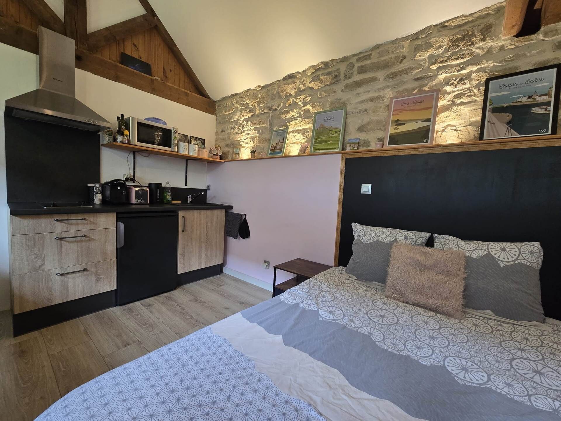 Un dormitorio compacto con cama, una kitchenette pequeña y una pared de piedra.