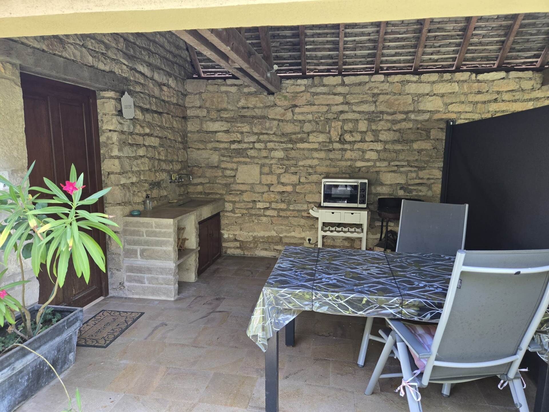 Eine Terrasse im Freien mit Steinwänden, einem Tisch, Stühlen, einem kleinen Spülbecken und einer Mikrowelle auf einem Holzboden.