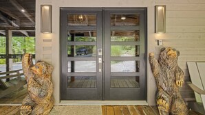 A double door entrance with a wooden porch, two bear sculptures, and wall-mounted lights.